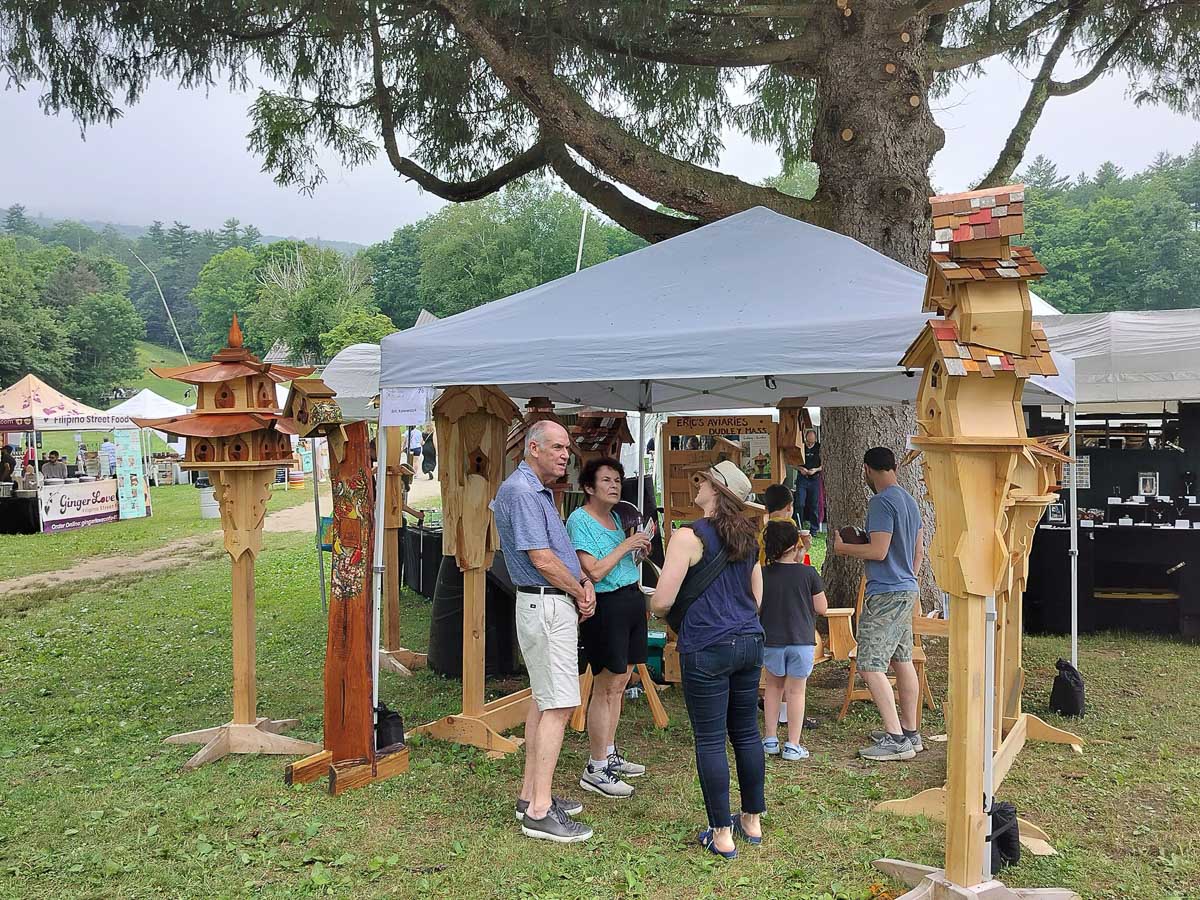 Event-goers visiting Eric's tent and admiring the arrangement of stained, painted, and natural wooden birdhouses.