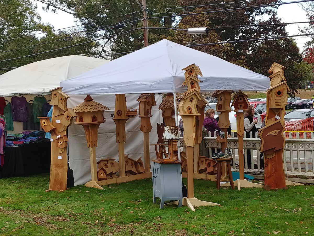 A collection of Eric's birdhouses and nesting boxes and whimsical furniture on display under an events tent.