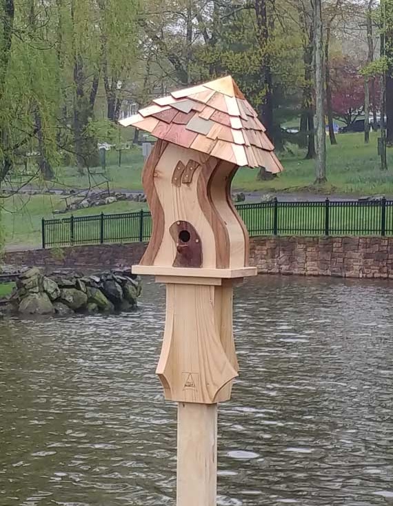 A wooden, Gumby style birdhouse curving uphill at a lakeside park.