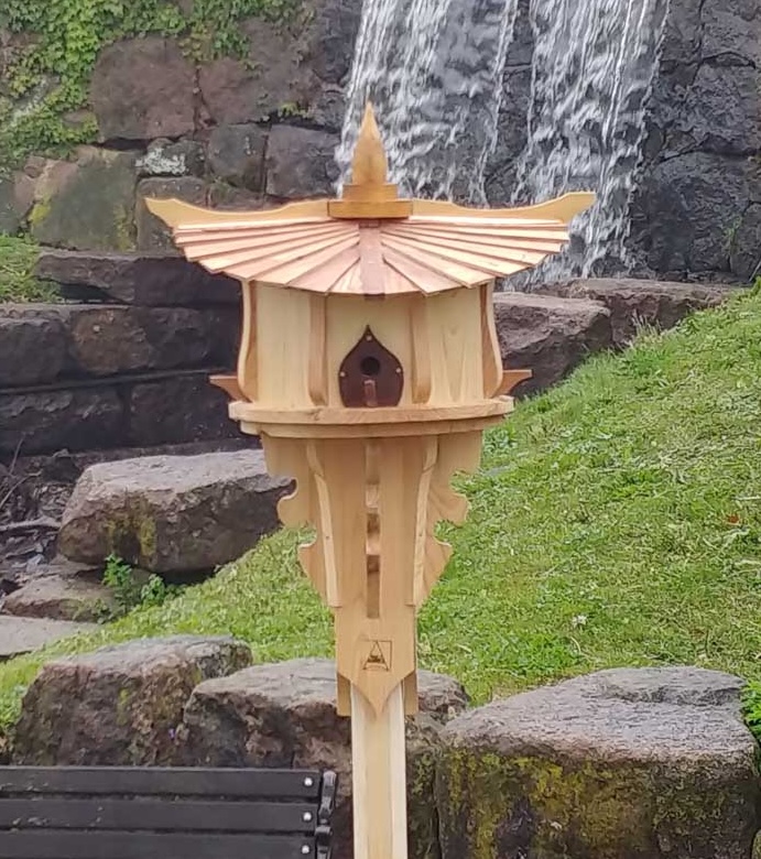 A wooden, Sunhouse style birdhouse standing proudly in front of a waterfall.